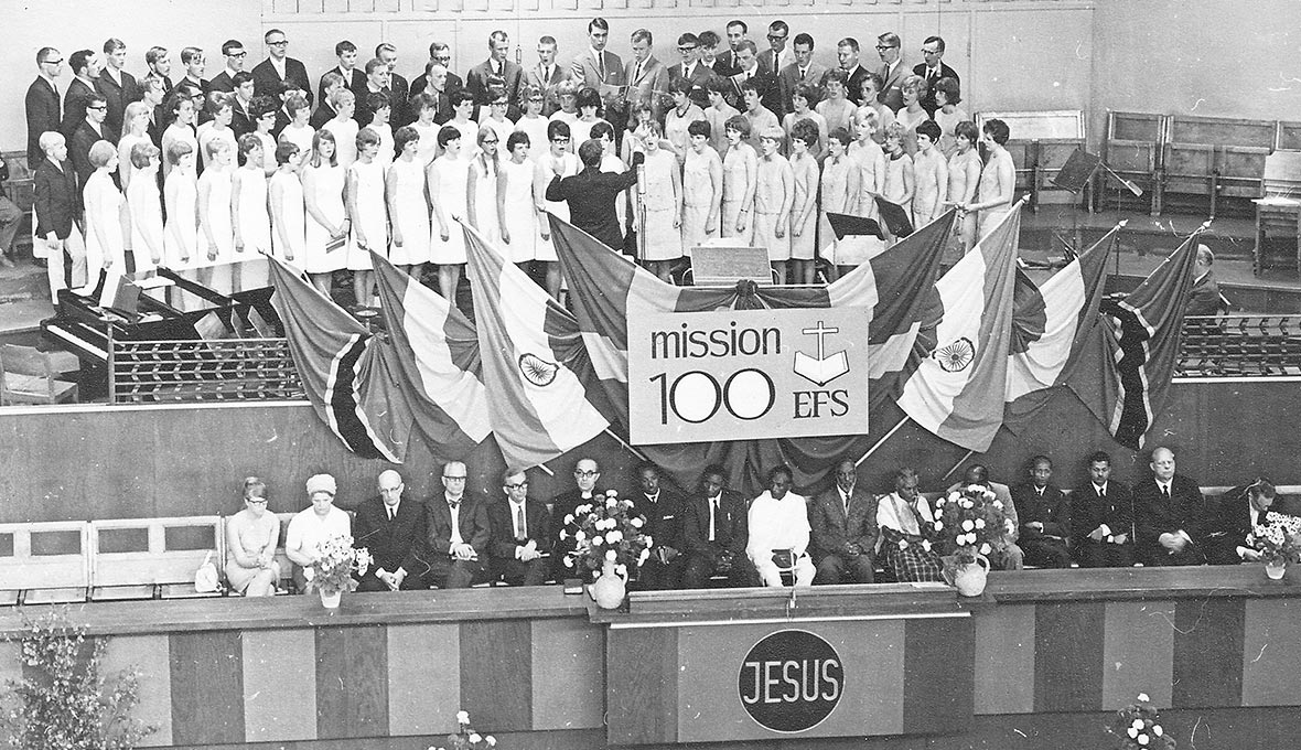 Körerna från Boliden och Norrfjärden sjunger under Eskil Lundströms ledning vid jubileumskonferens inledningsgudstjänst i Filadelfiakyrkan. På podiet sitter kvällens talare och de utländska gästerna.