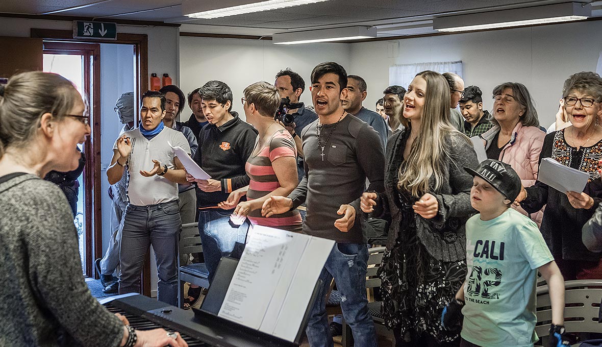 Körrepetition på Grytans flyktingförläggning 2016. The Rockin’ Pots körledare Tove Thofelt tar i från tårna och längst till höger står Mustafa tillsammans med sin vän Sarah.